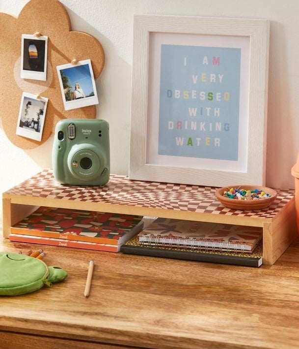 a desk riser on a wood desk with an assortment of decor and office supplies around it