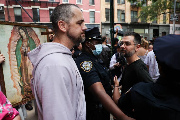Moscinski, a bearded man in a hoodie with a grim expression, stands amid a crowd of police and demonstrators