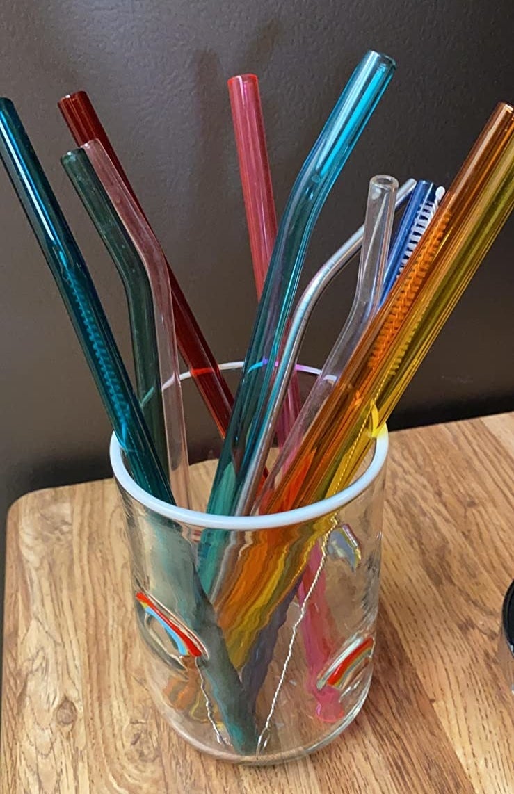 reviewer&#x27;s blue, pink, yellow, and orange transparent straws stored in a glass with their cleaning brush