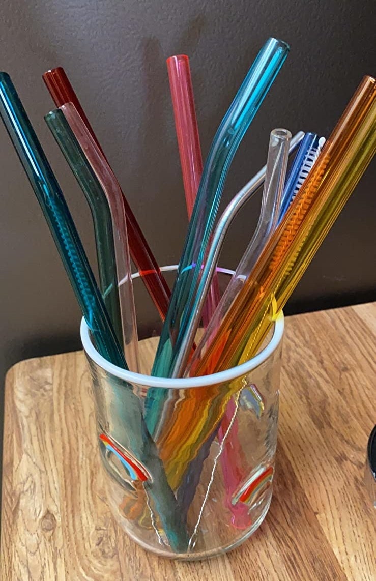reviewer's blue, pink, yellow, and orange transparent straws stored in a glass with their cleaning brush