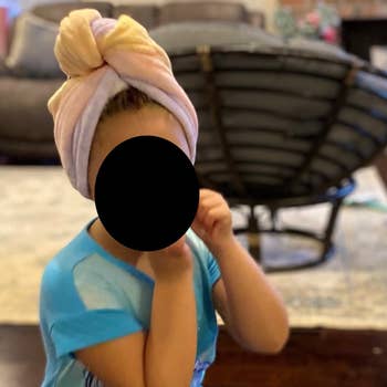 reviewer's child wearing the colorful hair drying wrap towel like a turban