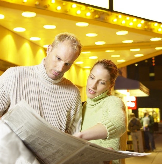 a couple looking at a newspaper at a movie theater