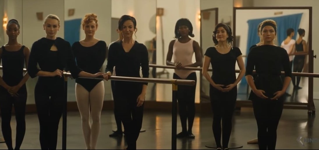 Seven women in black ballet outfits line up at the barre