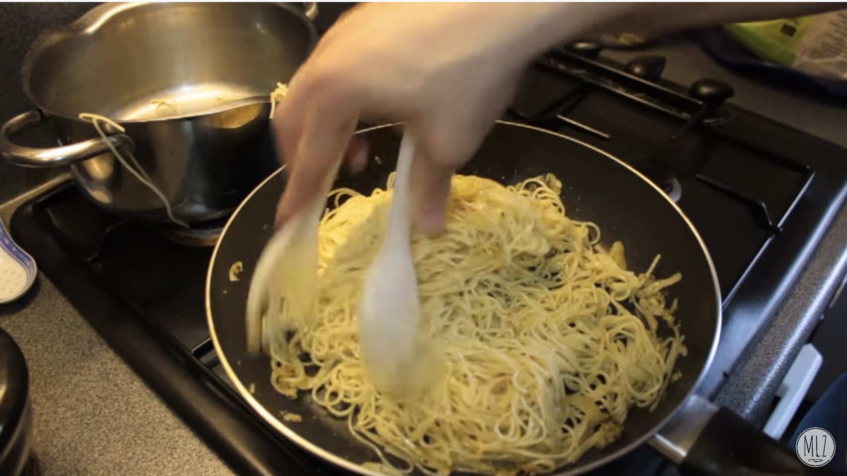 Person using tongs to pick up spaghetti in a pan