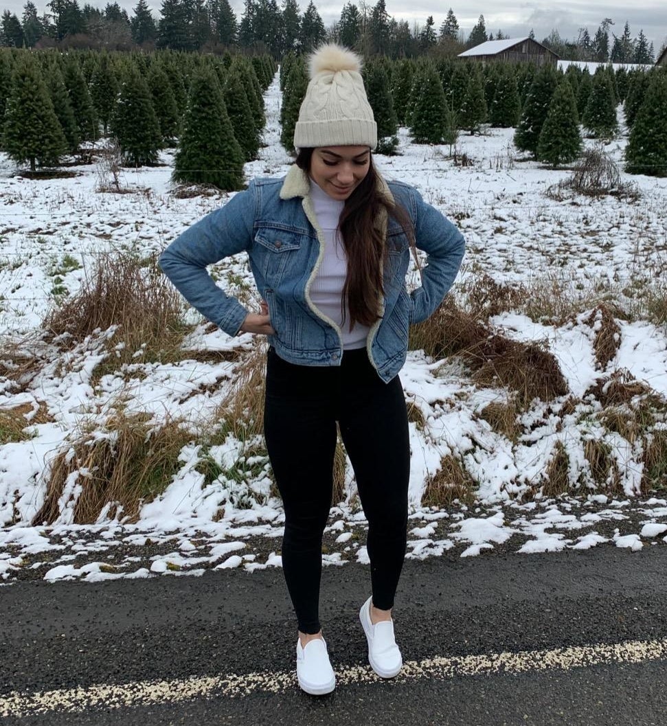Reviewer standing in front of snowy Christmas tree farm in the blue sherpa lined jacket, paired with leggings and hat