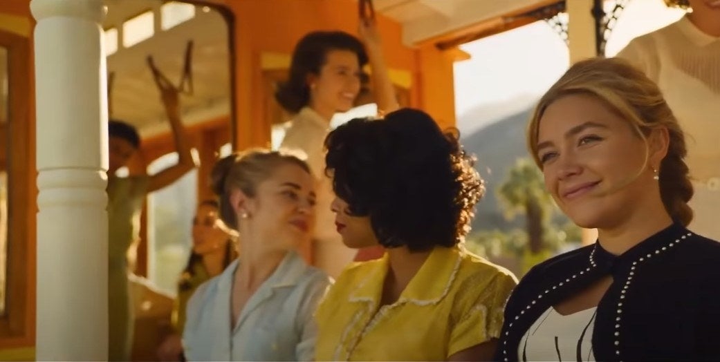 Alice smiling on a bus, surrounded by women in dresses