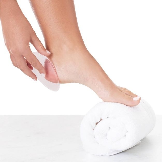 A person with their foot lace on a rolled white towel while using a foot polisher