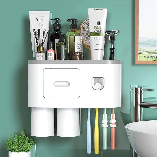 A white and grey plastic toothbrush holder with automatic toothpaste dispenser