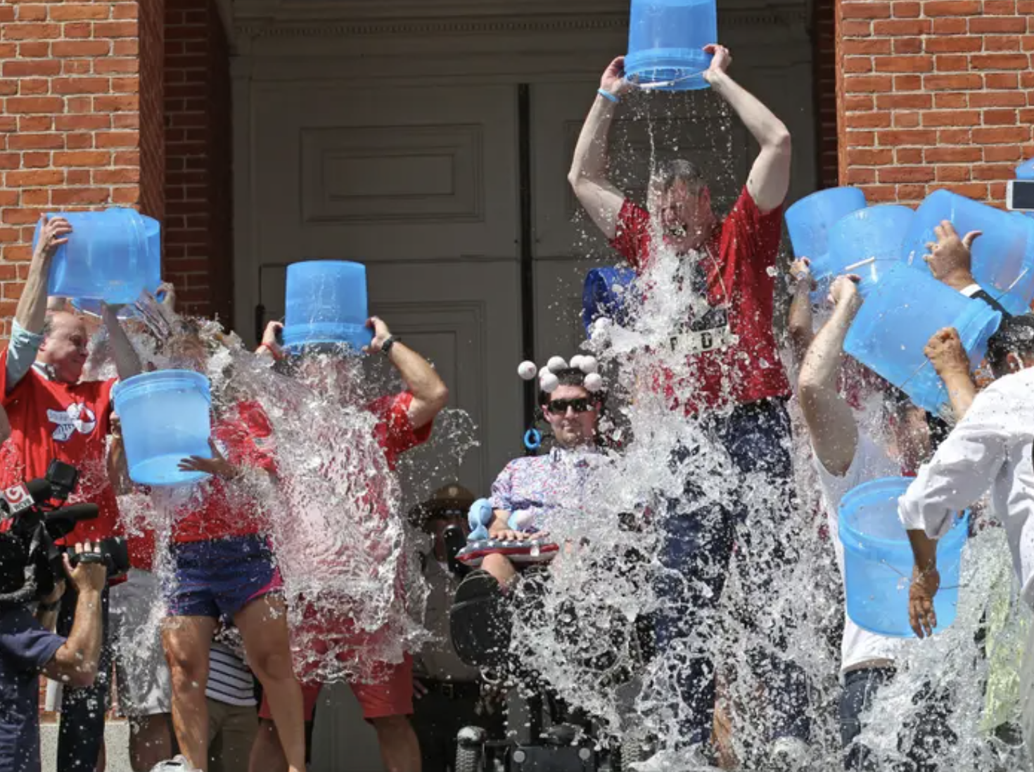 A bunch of people in red shirts dump blue buckets full of ice cold water over their head