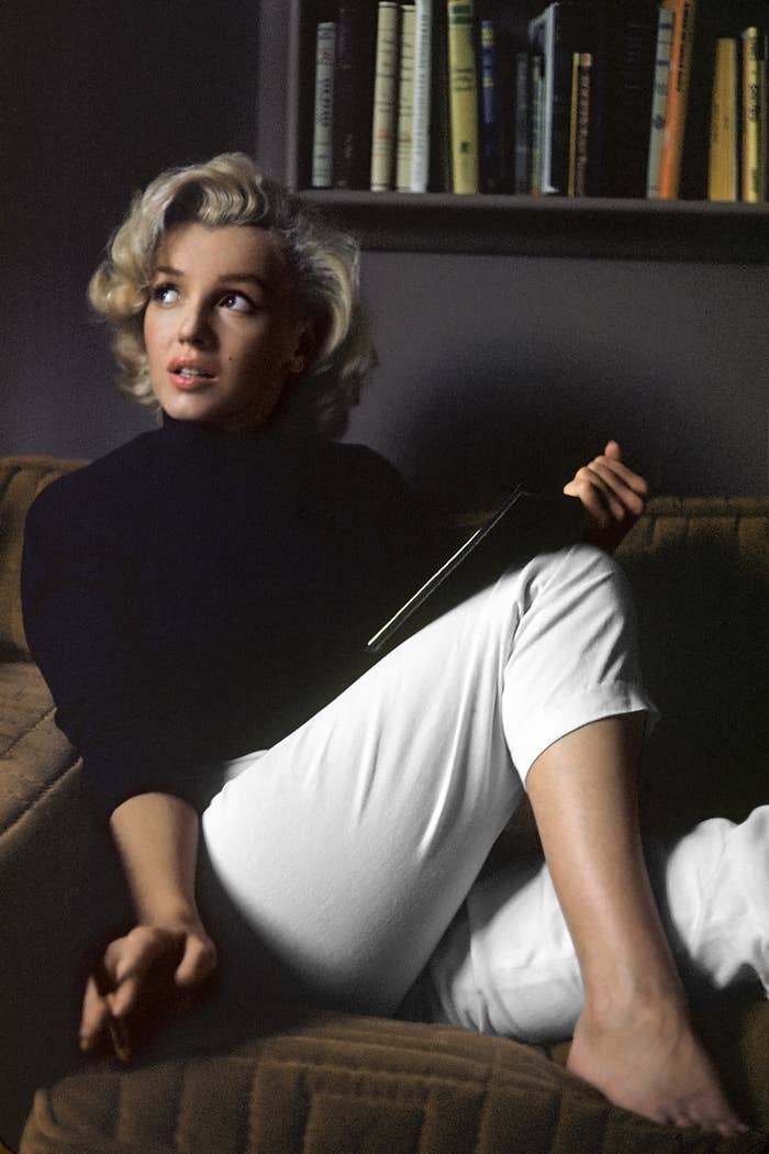 Marilyn sitting on a couch wearing cropped pants and holding a book