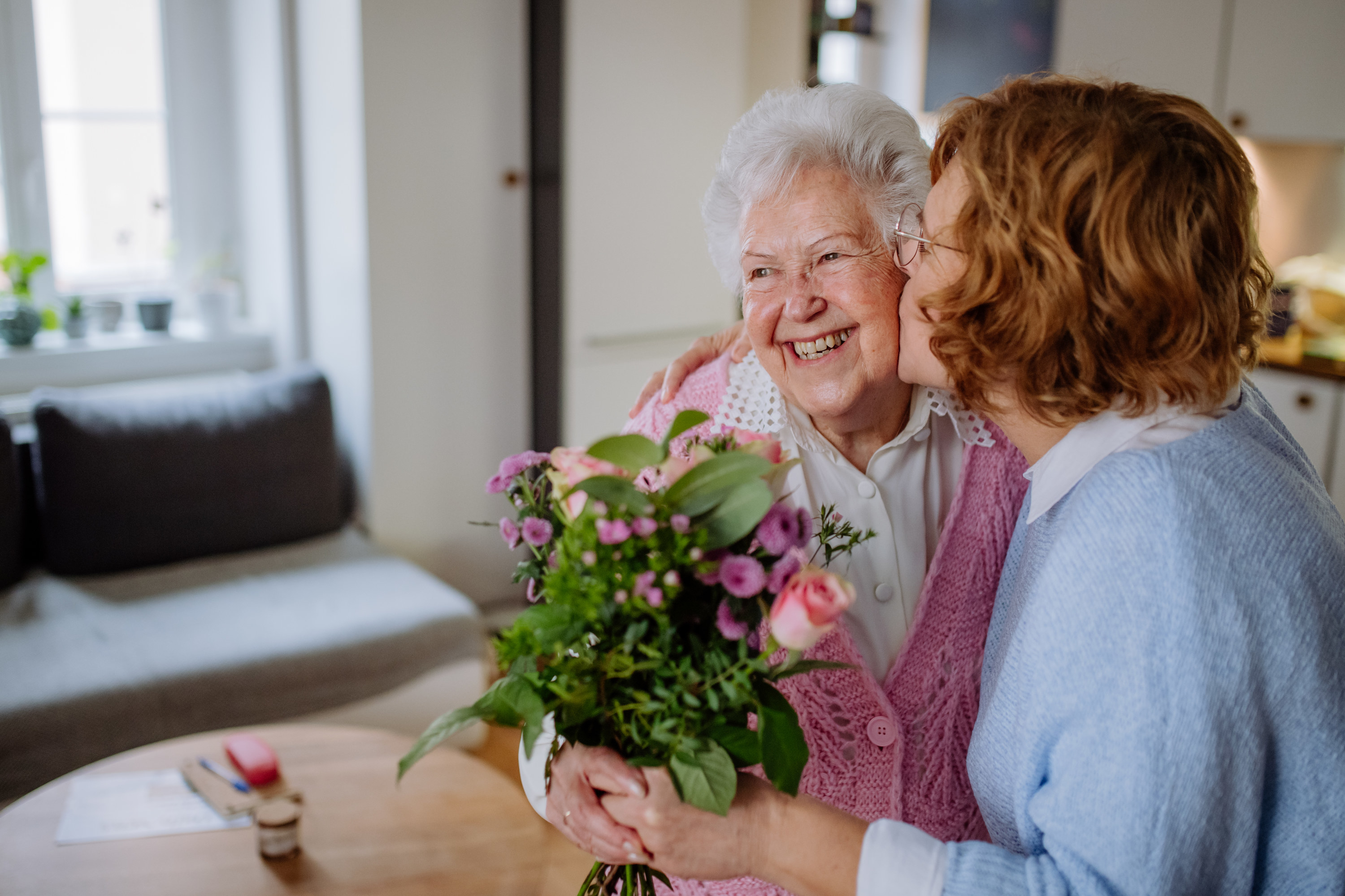 A person kissing a smiling older woman and giving her a bouquet of flowers