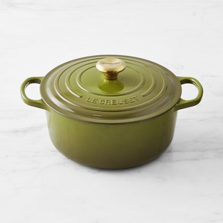 A green dutch oven with a gold handle on the top of the lid
