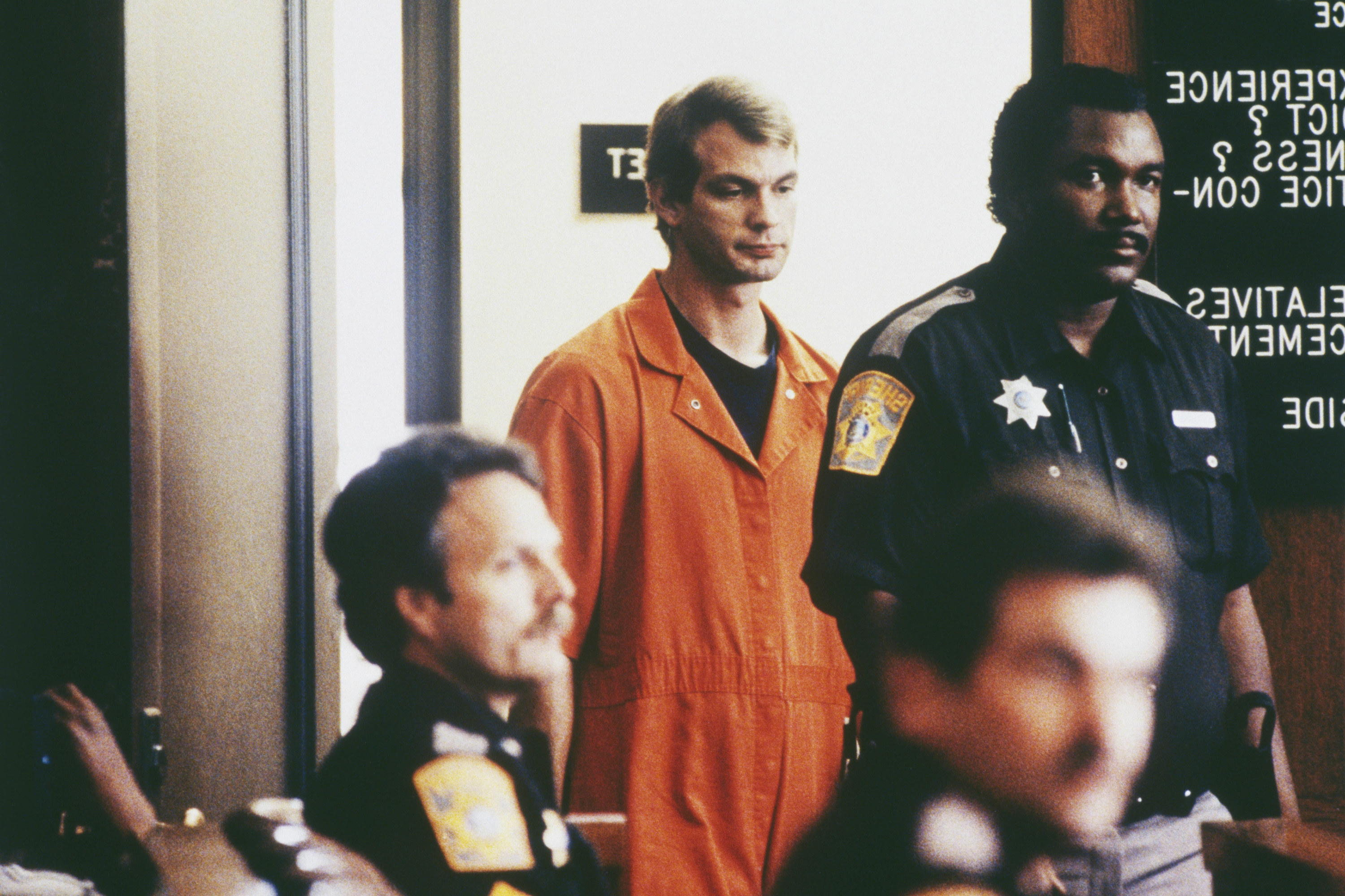 Dahmer in prison overalls alongside police officers