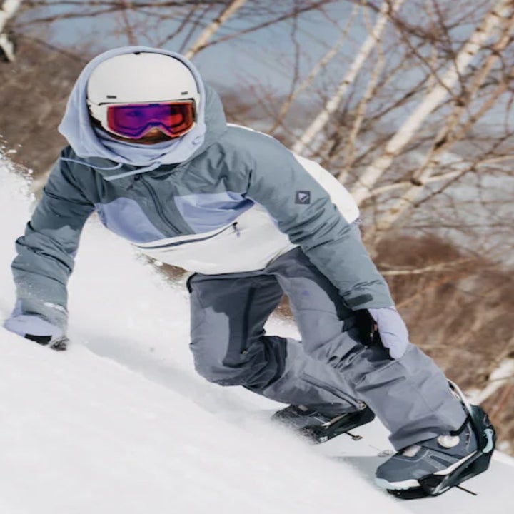 Model snowboarding down slope in the white grey and purple jacket