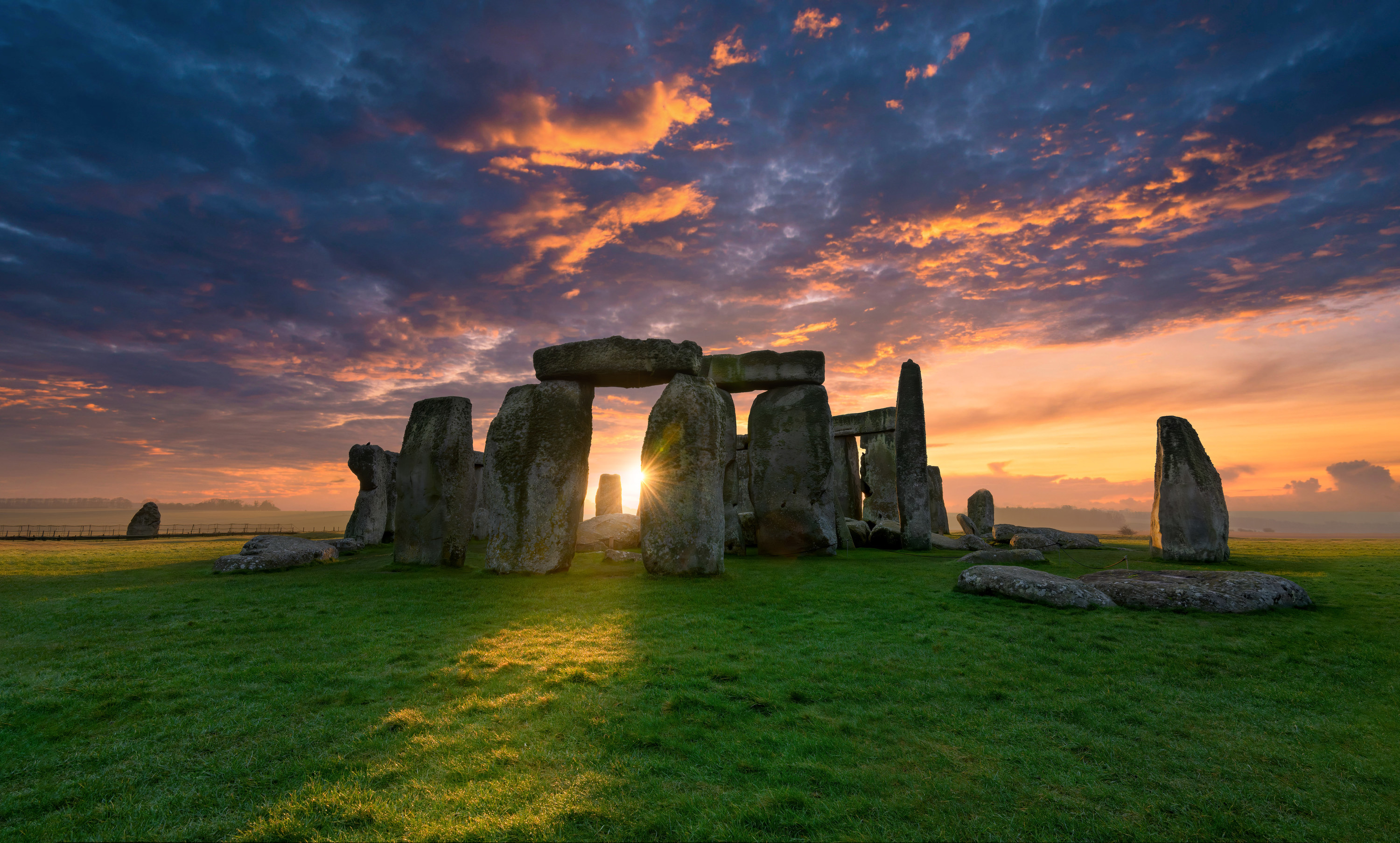 Stones of different sizes and heights surrounded by grass with sunlight behind them