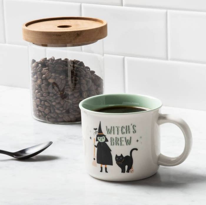 a white mug with an illustration of a witch and a cat and text that reads "witch's brew"