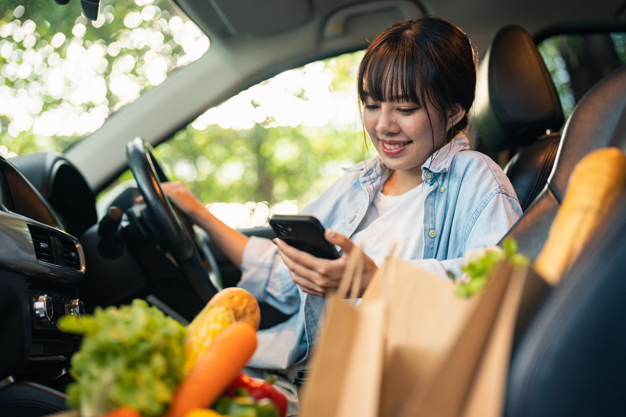 A woman sits in the car with her curbside pickup grocery order
