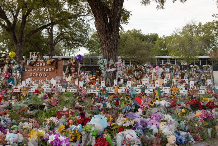 Stuffed animals, flowers, wreaths, and other decorations sit among crosses with victims&#x27; names on them