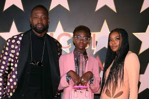 Dwyane Wade appears in a black suit while Zaya Wade wears a pink pantsuit with a matching bag and Gabrielle Union wears a melon-colored dress with cutouts and braids.