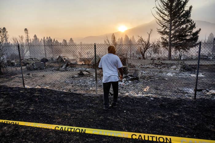 Man standing and looking at rubble, the remains of a burned house, with the sun over hills in the background