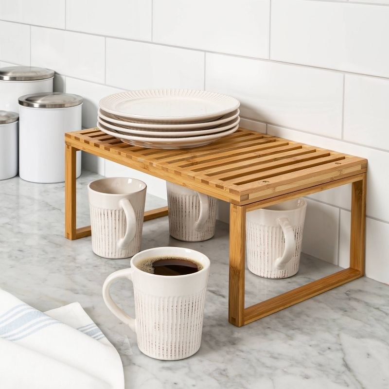 a stackable bamboo shelf holding mugs and dishes