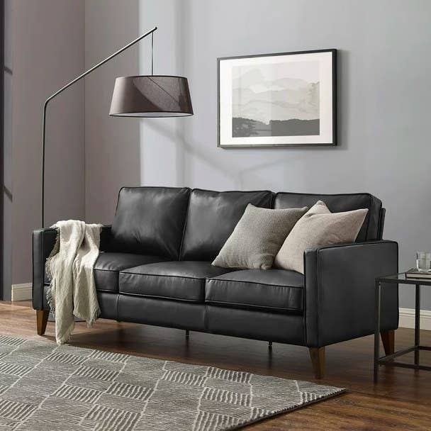 Black sofa with throw pillows and blanket on it in a gray living room