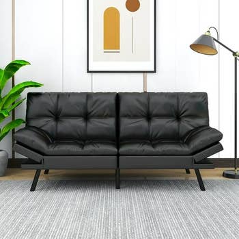 Black futon with floor lamp next to it and piece of art above it