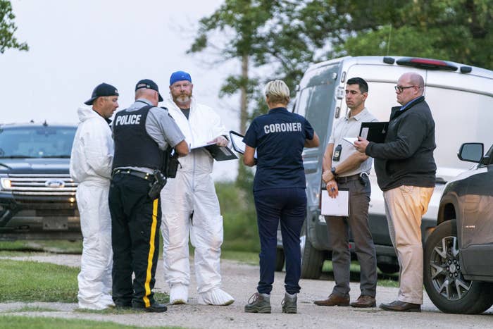 Six people, some wearing uniforms, stand together near vehicles