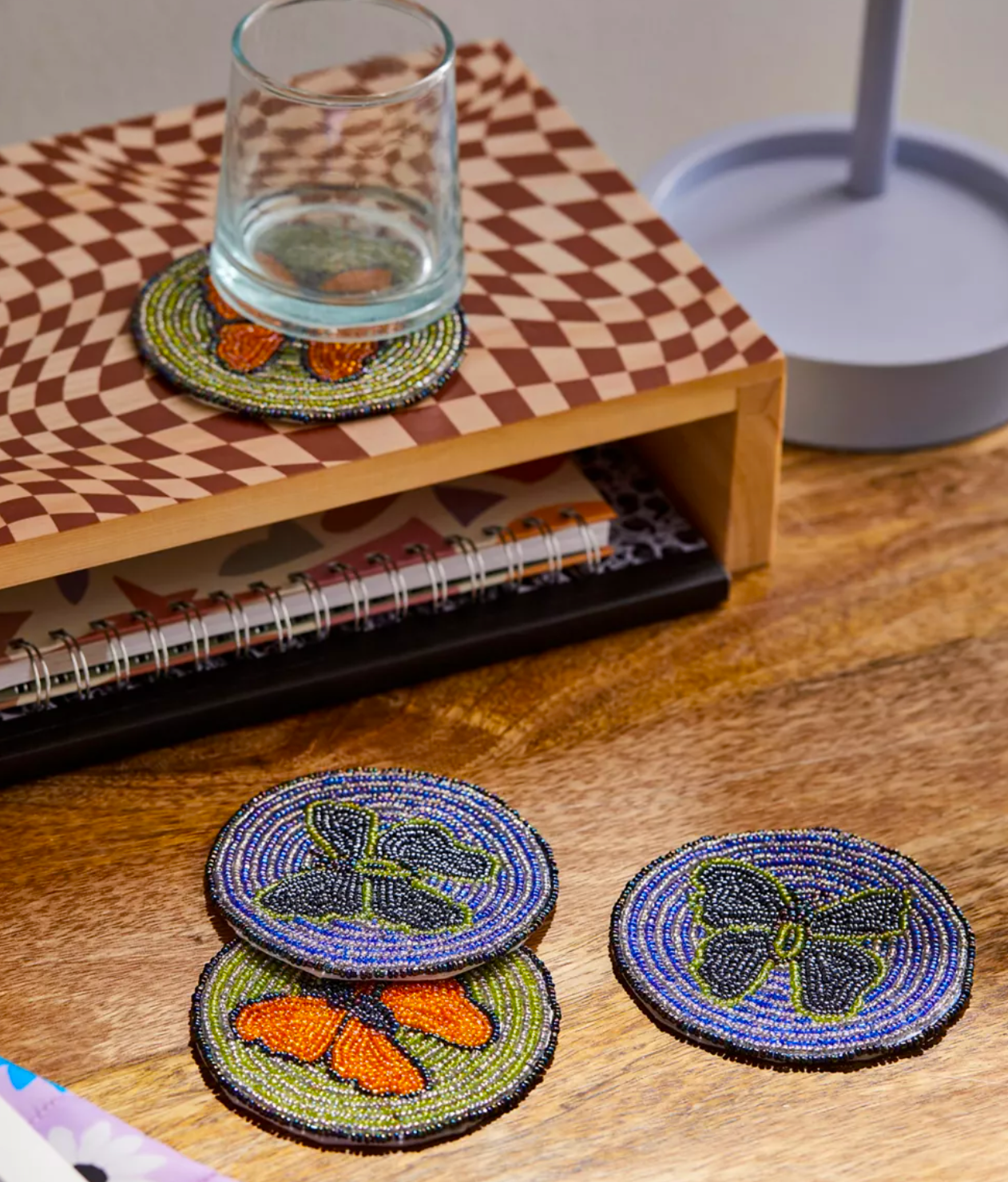 Four beaded coasters on a table, one with a glass on them