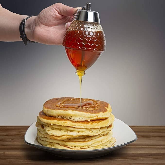 a person putting syrup on a stack of pancakes with the dispenser