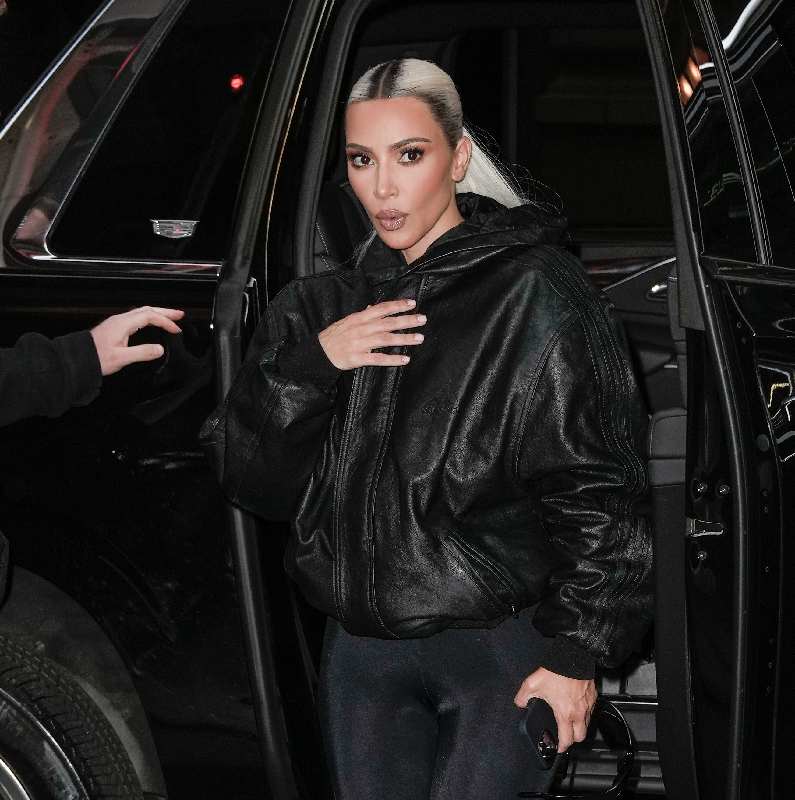 Kim in a leather jacket and emerging from a vehicle