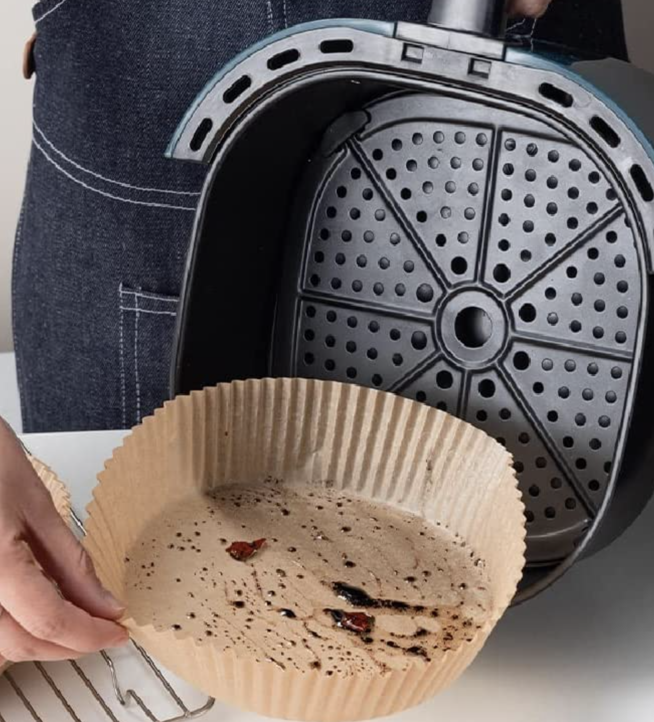 a person taking a messy liner out of a clean air fryer basket