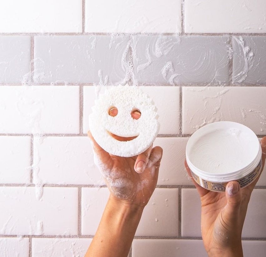 Person cleaning a tiled wall with a smiley face sponge.