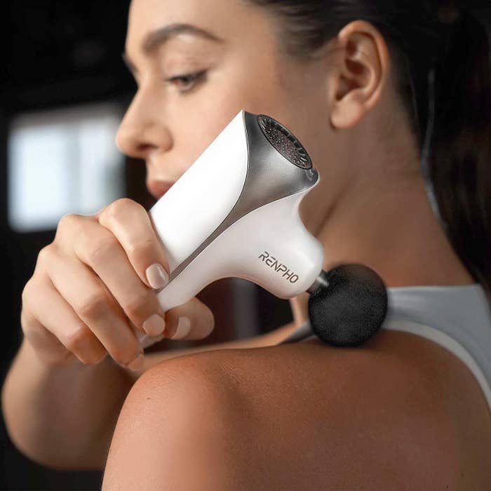 a person using the massage gun on their shoulder