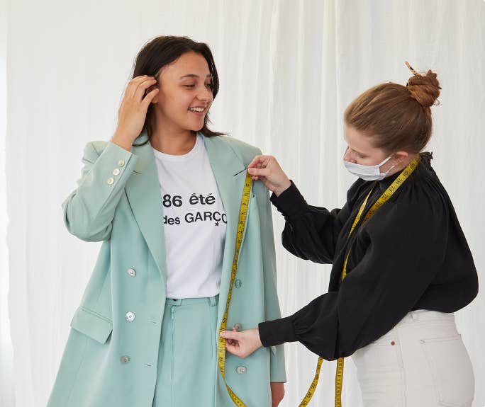 A model wearing a blazer which is being measured by a seamstress