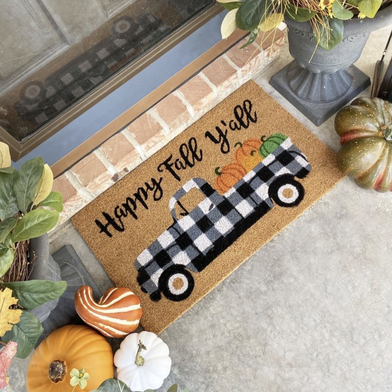 The doormat with plaid pickup truck with pumpkins in bed and the script above reading &quot;happy fall yall&quot;
