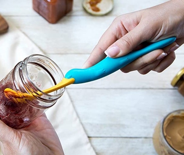 somebody using the spatula to get jam out of a jar