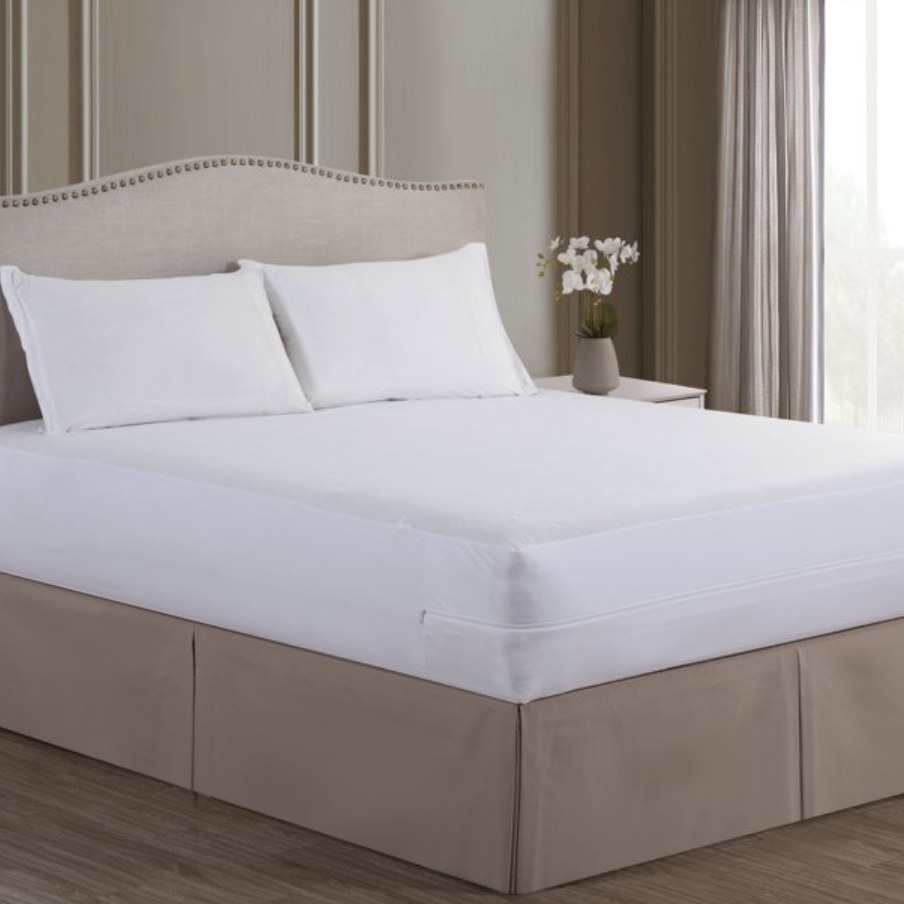 The mattress has a white zippered protector around it and two white pillows in a taupe-colored room