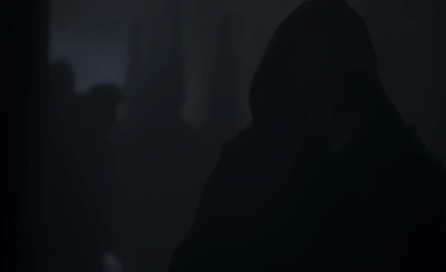 A hooded figure walks in the dark