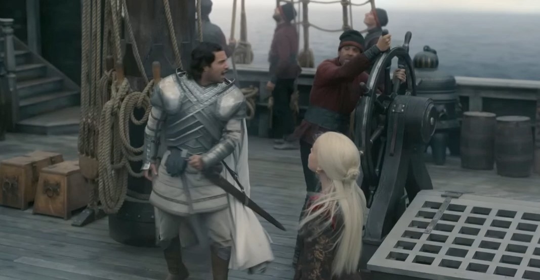 Rhaenyra looks up while standing on a ship; Ser Criston stands near her yelling at the nearby crew
