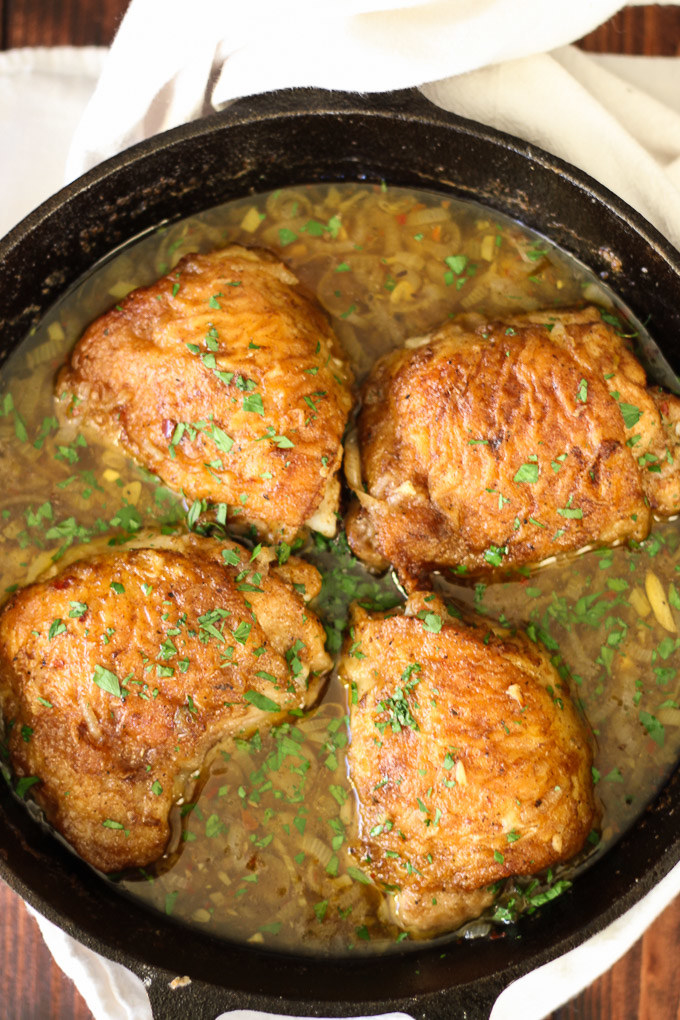 Skillet with four chicken breasts topped with green chopped herbs