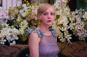 Daisy from The Great Gatsby sitting on a couch in front of loads of flowers