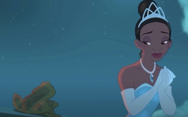 Tiana wears a tiara and gown and looks at a frog.