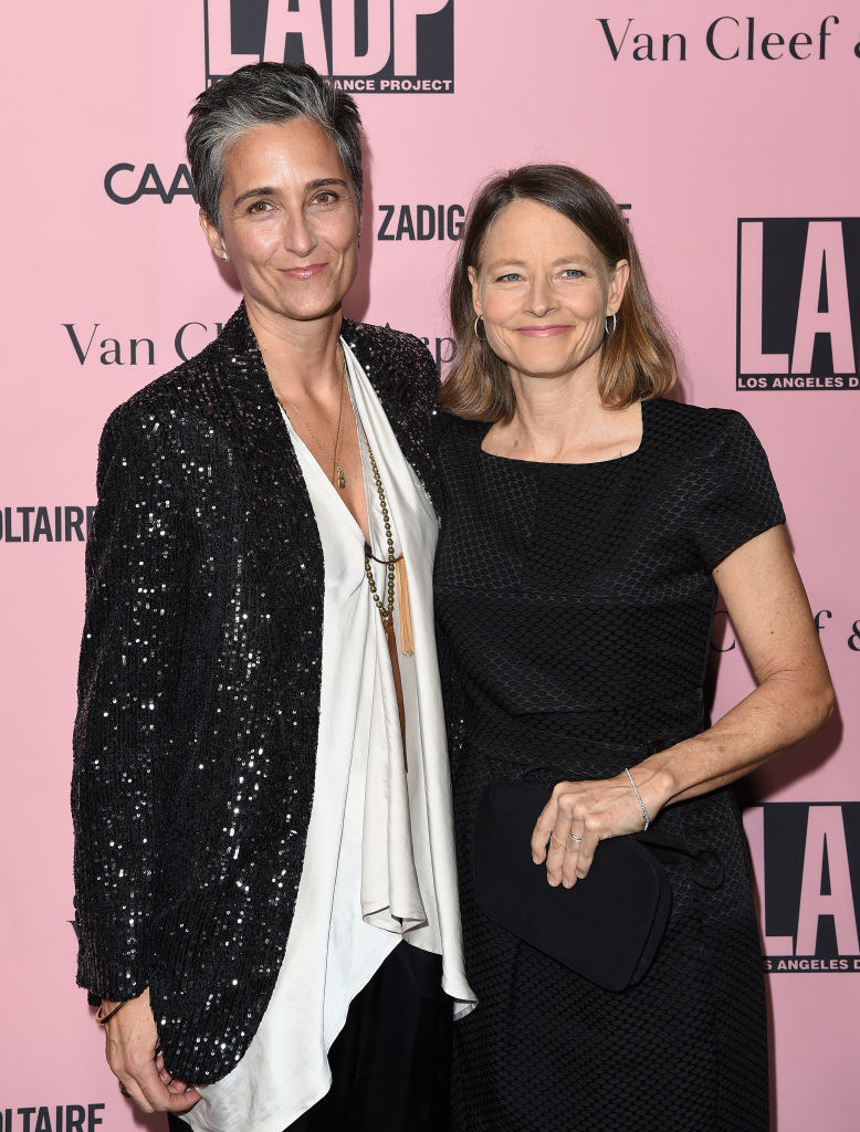 Alexandra Hedison wears a light colored blouse under a sparkly blazer and Jodie Foster wears a short sleeve dark dress