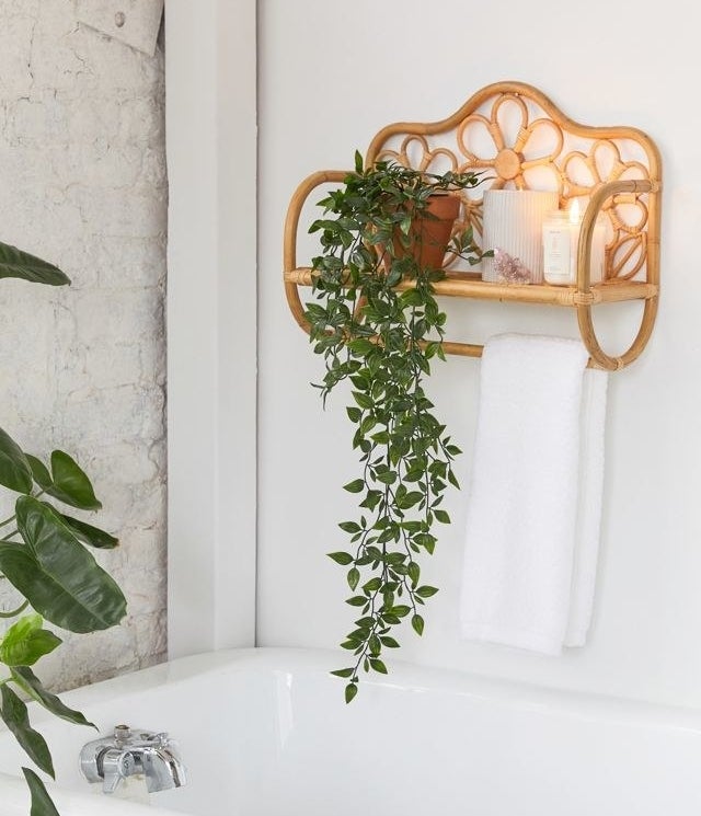 a rattan floral wall shelf with candles and a plant on it with a towel hanging from the bottom rack
