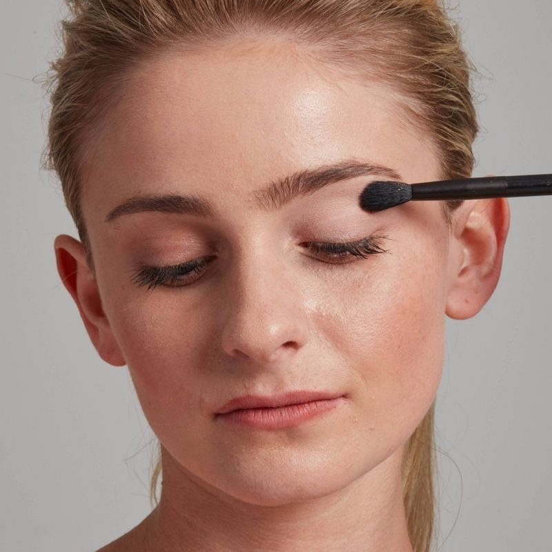 A person applying eyeshadow primer with a makeup brush