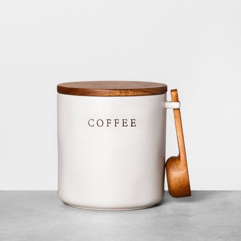 the white container with &#x27;COFFEE&quot; stamped on the side, a wooden lid and a wooden scoop attached to the side