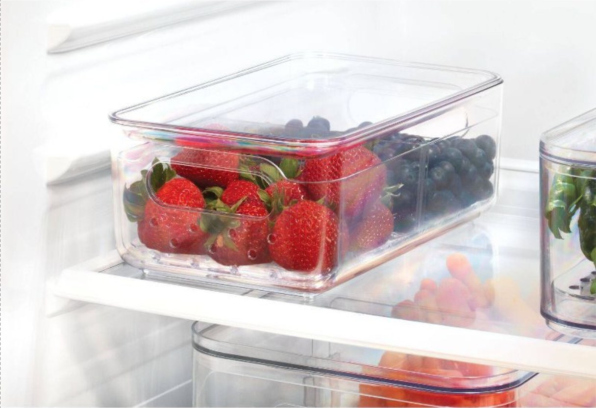 the clear bin in a fridge, filled half with strawberries and half with blueberries