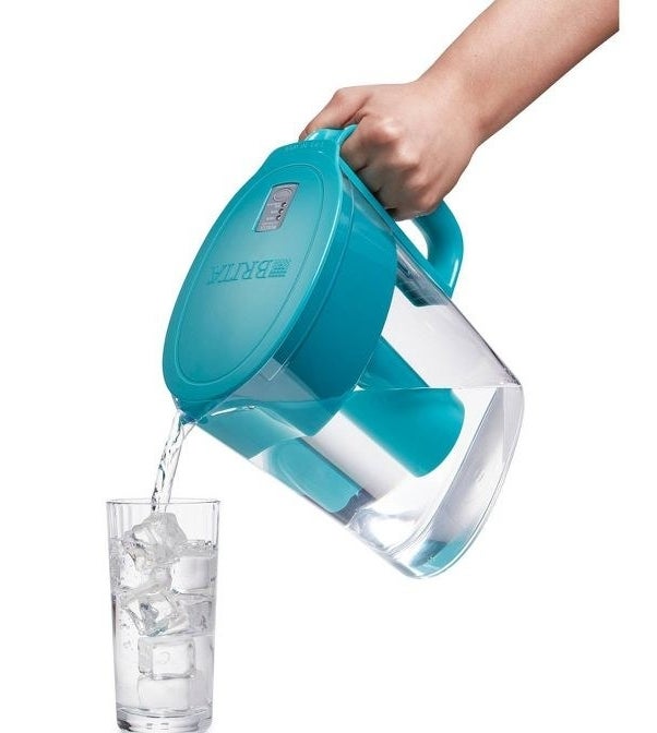 a hand pouring water into a glass out of the turquoise pitcher