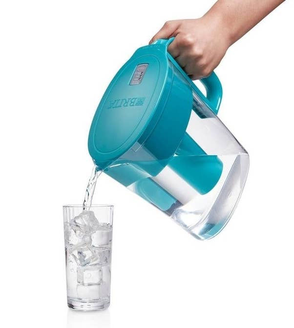 a hand pouring water into a glass out of the turquoise pitcher